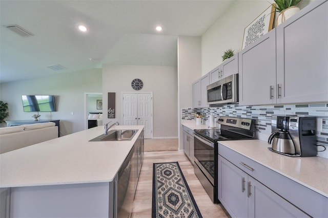 kitchen featuring appliances with stainless steel finishes, sink, light hardwood / wood-style floors, vaulted ceiling, and a kitchen island with sink