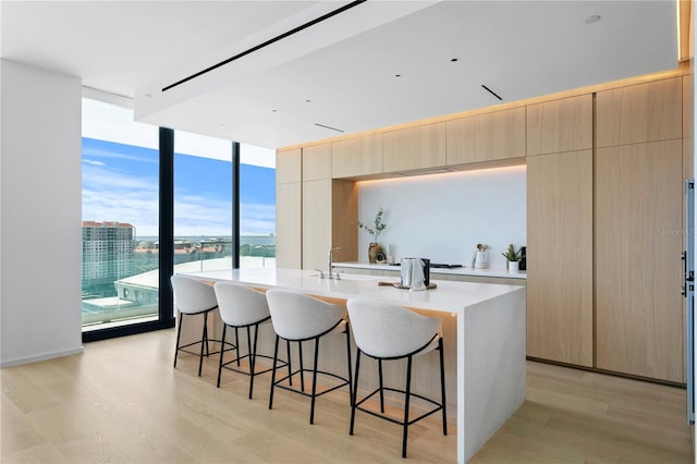 kitchen featuring light brown cabinetry, a kitchen bar, a center island with sink, and light wood-type flooring