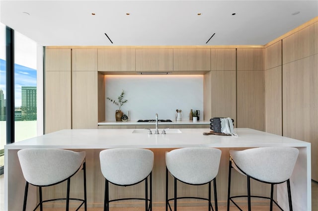 kitchen with white gas cooktop, light brown cabinetry, and a kitchen island with sink