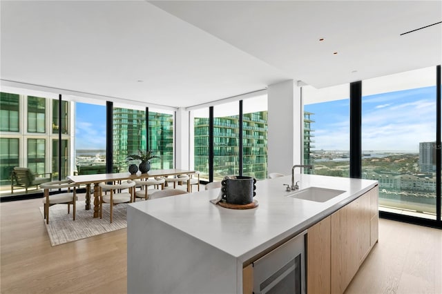 kitchen with a center island with sink, expansive windows, sink, light hardwood / wood-style floors, and beverage cooler