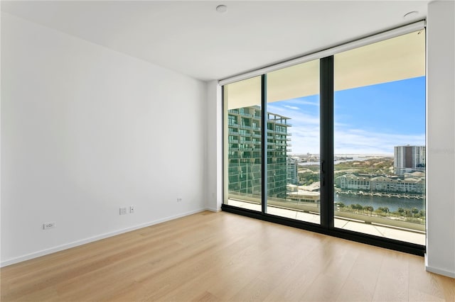 spare room featuring a water view, a wall of windows, and light hardwood / wood-style floors