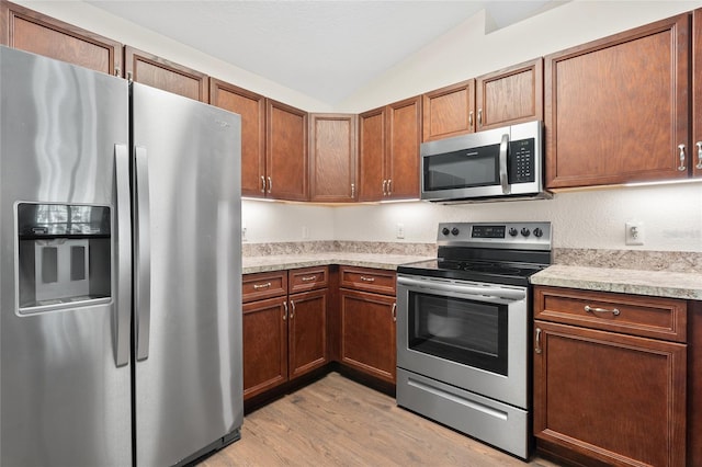 kitchen featuring light hardwood / wood-style floors, lofted ceiling, stainless steel appliances, and light stone counters