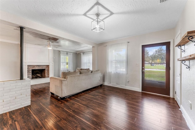 living room with a stone fireplace, a textured ceiling, a healthy amount of sunlight, and dark hardwood / wood-style flooring