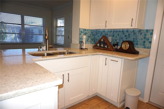 kitchen with white cabinetry, sink, decorative backsplash, light hardwood / wood-style floors, and crown molding