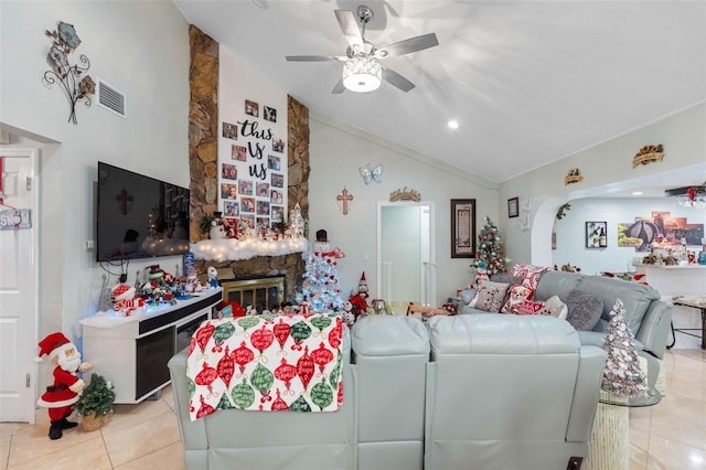 living room with vaulted ceiling, ceiling fan, a stone fireplace, and light tile patterned flooring