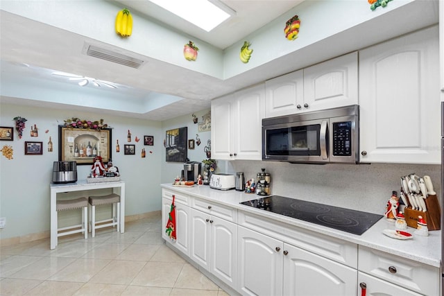 kitchen featuring white cabinetry, black electric cooktop, light tile patterned floors, and a tray ceiling