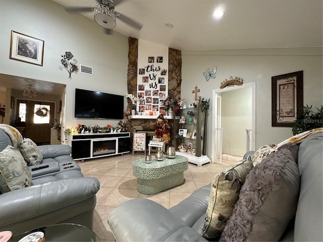 living area featuring light tile patterned floors, visible vents, a ceiling fan, a stone fireplace, and high vaulted ceiling