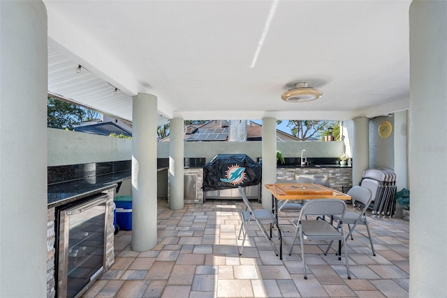 view of patio with beverage cooler, a sink, outdoor dining area, and an outdoor kitchen