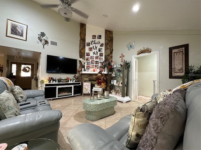living room with light tile patterned floors, visible vents, a ceiling fan, high vaulted ceiling, and a lit fireplace