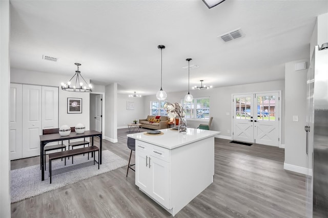 kitchen featuring white cabinetry, light wood-type flooring, french doors, decorative light fixtures, and a center island