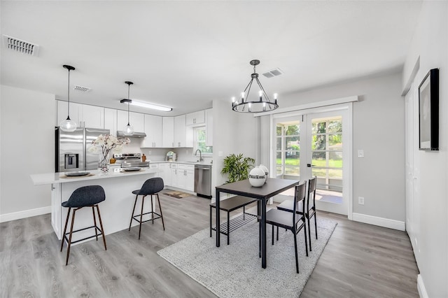 dining space with light hardwood / wood-style floors, french doors, sink, and a notable chandelier