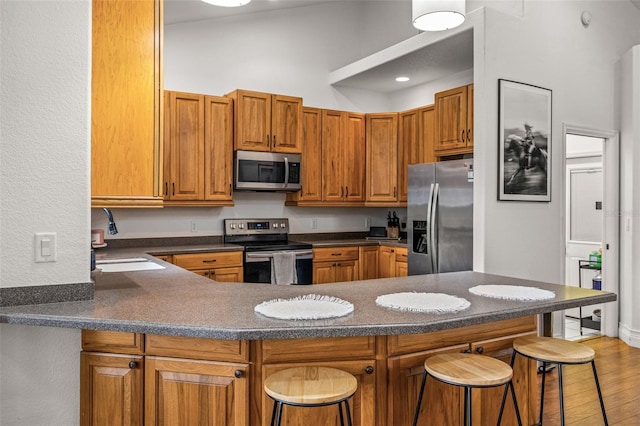 kitchen featuring wood-type flooring, sink, kitchen peninsula, stainless steel appliances, and a breakfast bar area