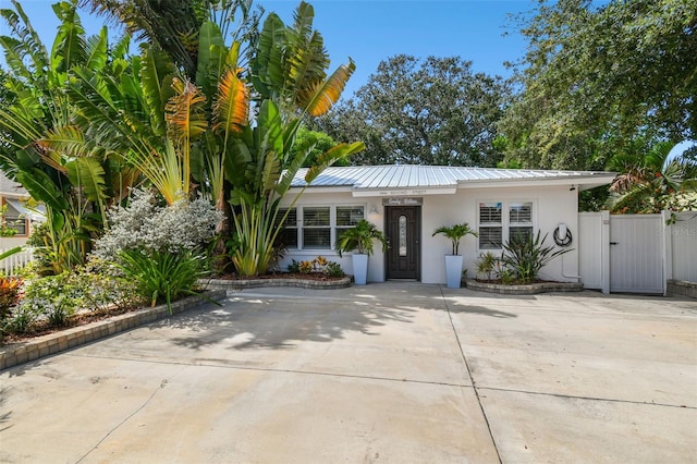 view of front facade with stucco siding, a gate, metal roof, and driveway