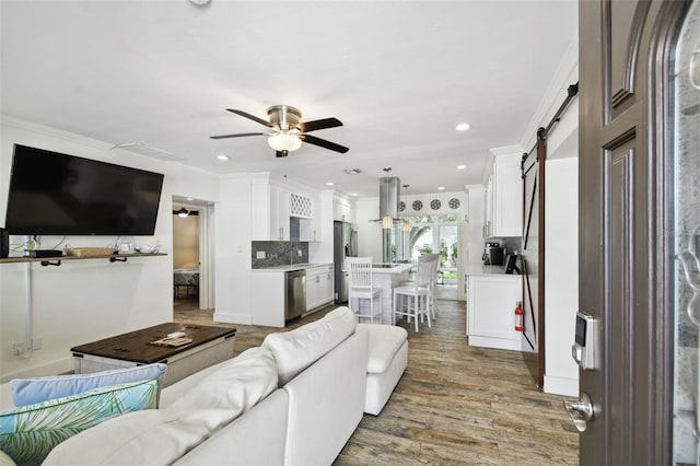 living room with ornamental molding, a barn door, hardwood / wood-style flooring, and ceiling fan