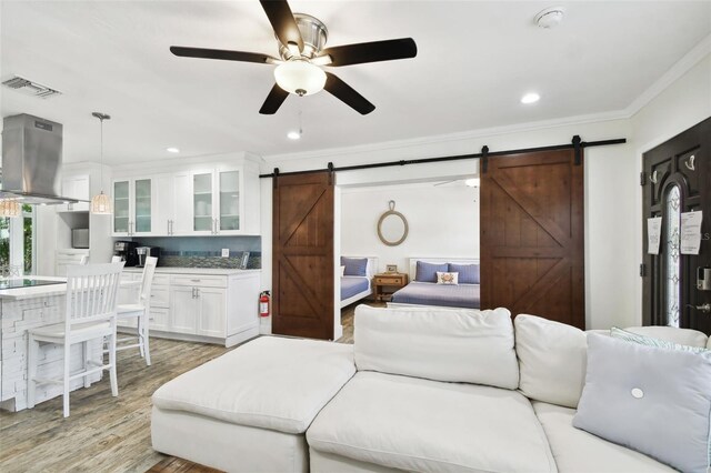 living room featuring a barn door, crown molding, ceiling fan, light wood-style flooring, and recessed lighting