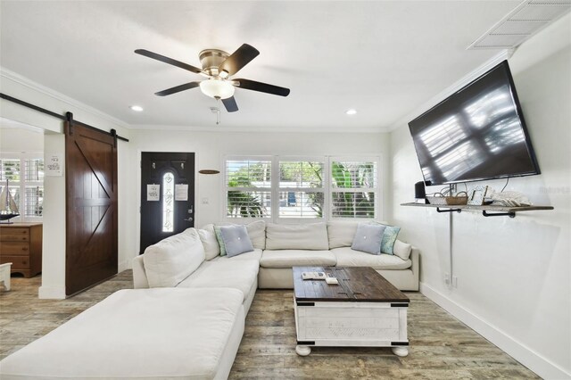 living room with a barn door, ceiling fan, ornamental molding, wood finished floors, and recessed lighting
