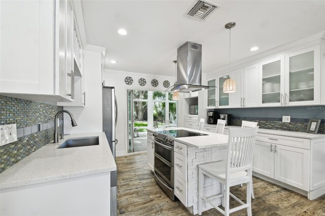 kitchen with a sink, stainless steel appliances, island exhaust hood, white cabinetry, and ornamental molding
