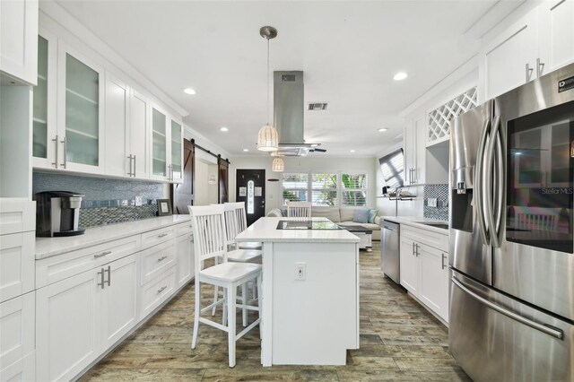 kitchen featuring stainless steel appliances, a barn door, backsplash, white cabinets, and recessed lighting