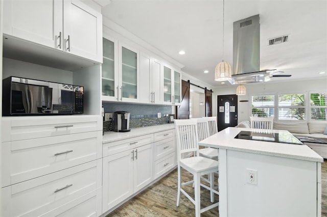 kitchen with light wood-type flooring, a barn door, a center island, hanging light fixtures, and white cabinets