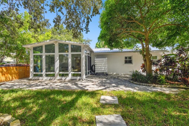 rear view of house with a sunroom, a patio area, stucco siding, and metal roof