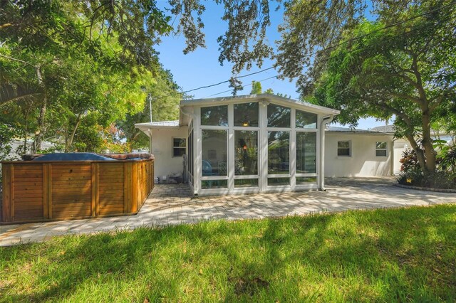 back of property with stucco siding, a patio, a sunroom, and a hot tub