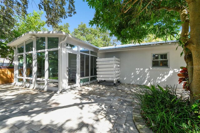 back of house featuring a sunroom, a patio area, stucco siding, and metal roof