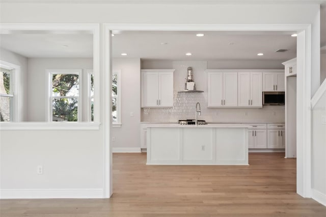 kitchen with stainless steel appliances, white cabinetry, wall chimney range hood, and light wood-type flooring