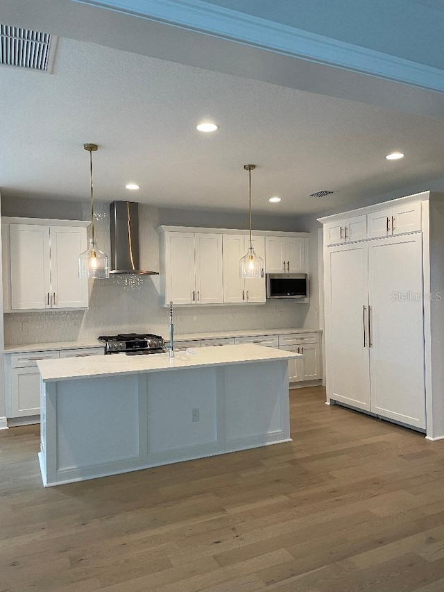 kitchen with white cabinetry, appliances with stainless steel finishes, wall chimney exhaust hood, and hanging light fixtures