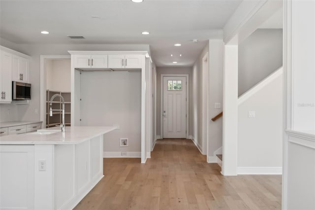 kitchen featuring an island with sink, sink, white cabinets, and light hardwood / wood-style flooring