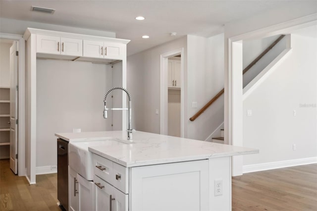 kitchen with sink, white cabinetry, light stone counters, light hardwood / wood-style floors, and a center island with sink