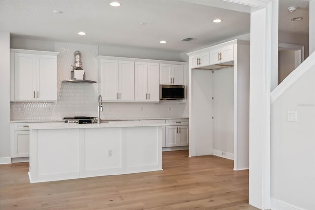 kitchen featuring white cabinetry, a kitchen island with sink, light hardwood / wood-style flooring, and wall chimney range hood