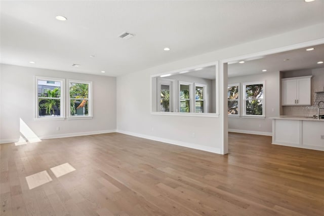 unfurnished living room with sink, a wealth of natural light, and light wood-type flooring