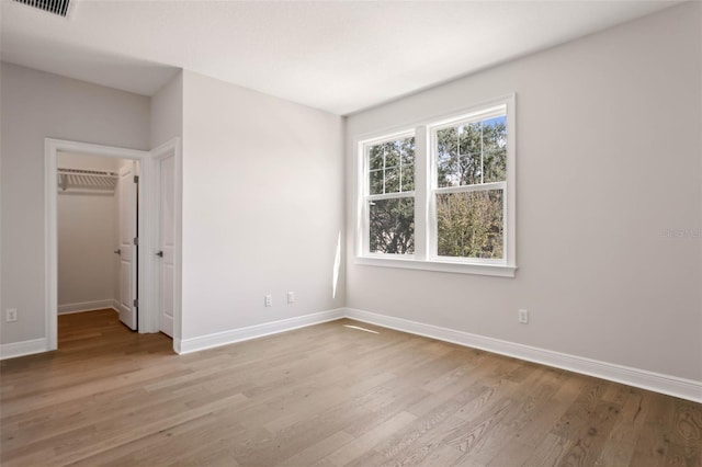 unfurnished bedroom with a wall mounted air conditioner, a spacious closet, a closet, and light wood-type flooring