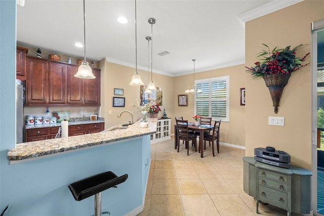 kitchen featuring light stone countertops, sink, hanging light fixtures, ornamental molding, and light tile patterned floors