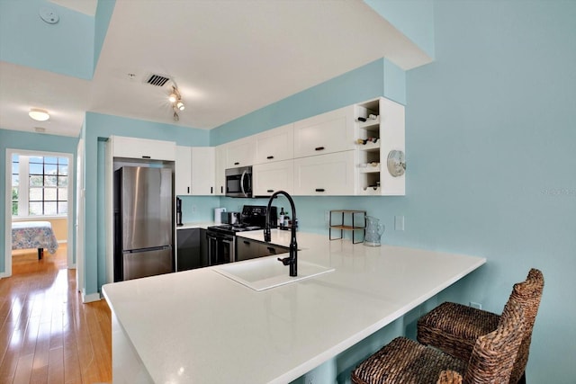 kitchen featuring stainless steel appliances, a kitchen breakfast bar, kitchen peninsula, light hardwood / wood-style floors, and white cabinets