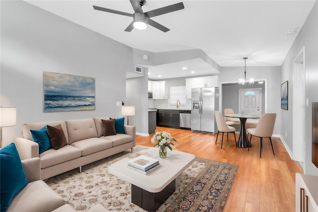 living room featuring lofted ceiling, sink, ceiling fan with notable chandelier, and light wood-type flooring