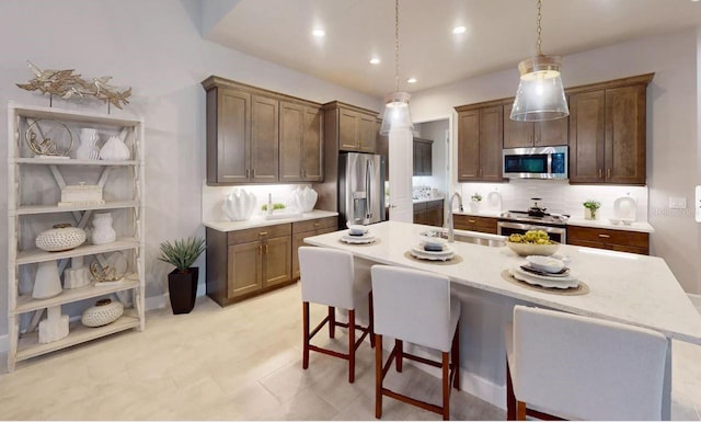 kitchen featuring a center island with sink, appliances with stainless steel finishes, decorative light fixtures, decorative backsplash, and sink