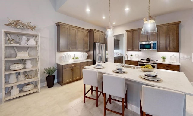 kitchen with appliances with stainless steel finishes, hanging light fixtures, sink, a breakfast bar area, and a kitchen island with sink