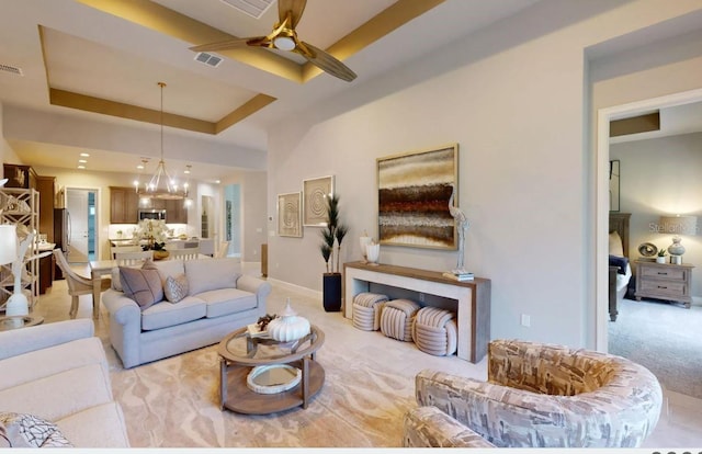 living room with ceiling fan with notable chandelier, light carpet, and a raised ceiling