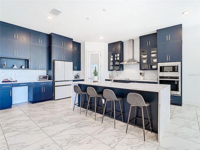 kitchen featuring a kitchen island with sink, a breakfast bar area, stainless steel appliances, wall chimney exhaust hood, and backsplash