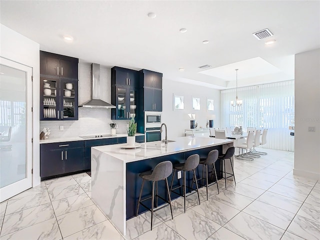 kitchen featuring stainless steel appliances, a center island with sink, a kitchen breakfast bar, and wall chimney exhaust hood