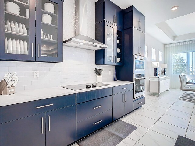 kitchen featuring appliances with stainless steel finishes, light stone countertops, wall chimney range hood, blue cabinets, and tasteful backsplash