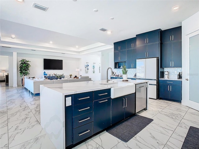 kitchen with sink, blue cabinets, white fridge, an island with sink, and stainless steel dishwasher