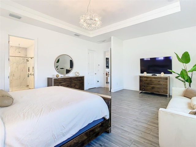 bedroom featuring hardwood / wood-style floors, a raised ceiling, ensuite bath, a chandelier, and ornamental molding