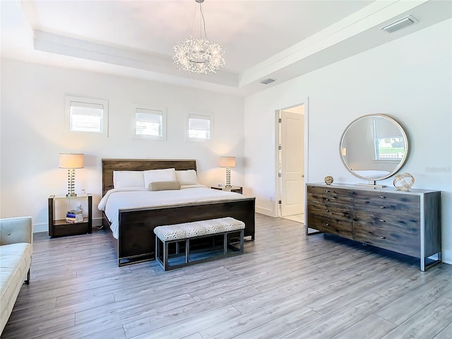 bedroom featuring light wood-type flooring, a raised ceiling, and a notable chandelier