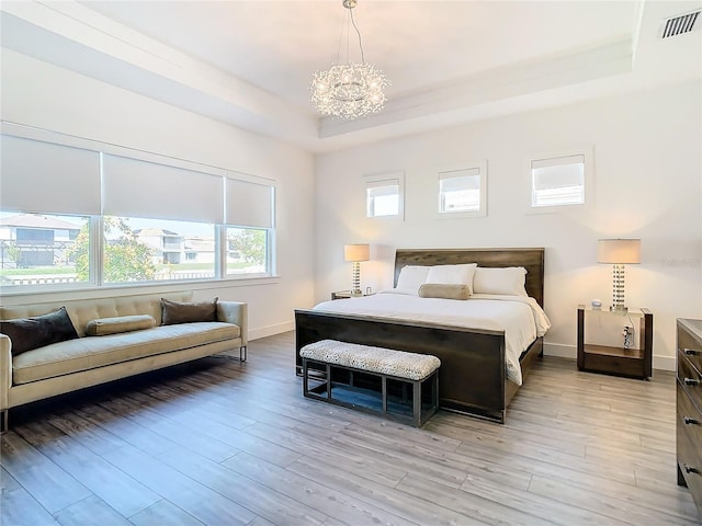 bedroom featuring a raised ceiling, light wood-type flooring, and a chandelier