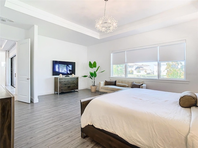 bedroom with wood-type flooring, multiple windows, a chandelier, and a tray ceiling