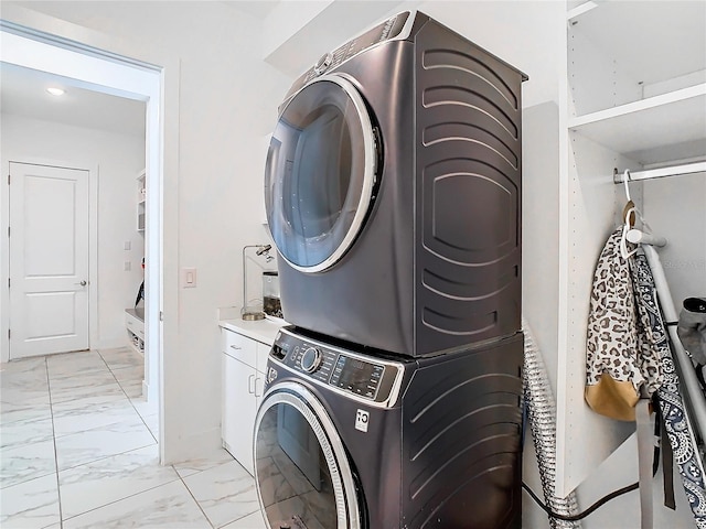 clothes washing area with stacked washer / drying machine and cabinets