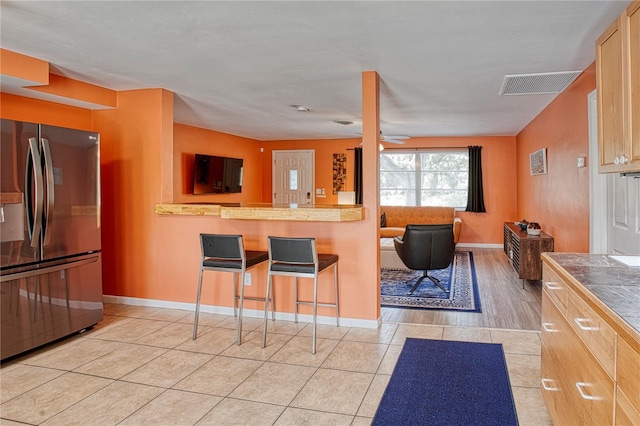 kitchen featuring stainless steel fridge, light brown cabinetry, light tile patterned floors, tile counters, and a breakfast bar area