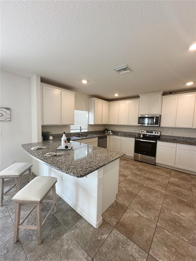 kitchen with a textured ceiling, white cabinets, stainless steel appliances, and a kitchen bar